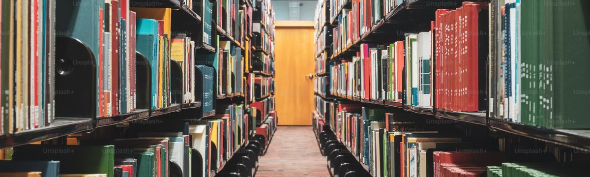 Long library aisle lined with shelves full of books leading to a closed wooden door