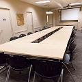 Square of tables lined with chairs white board on one wall, screen on back wall