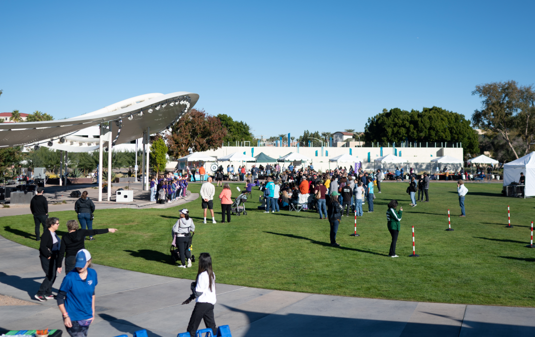 Crowd gathered on a grassy lawn next to an outdoor stage and event tents.