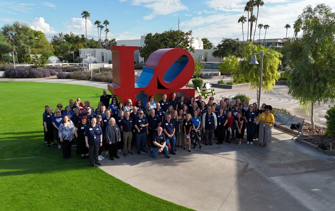 Large group of people posing outdoors in front of a red LOVE sculpture.