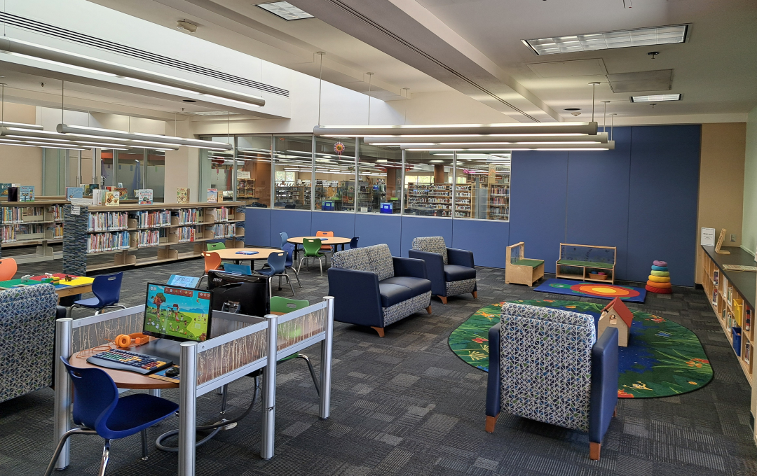 Library children's area with computer desks, seating, and a play rug.