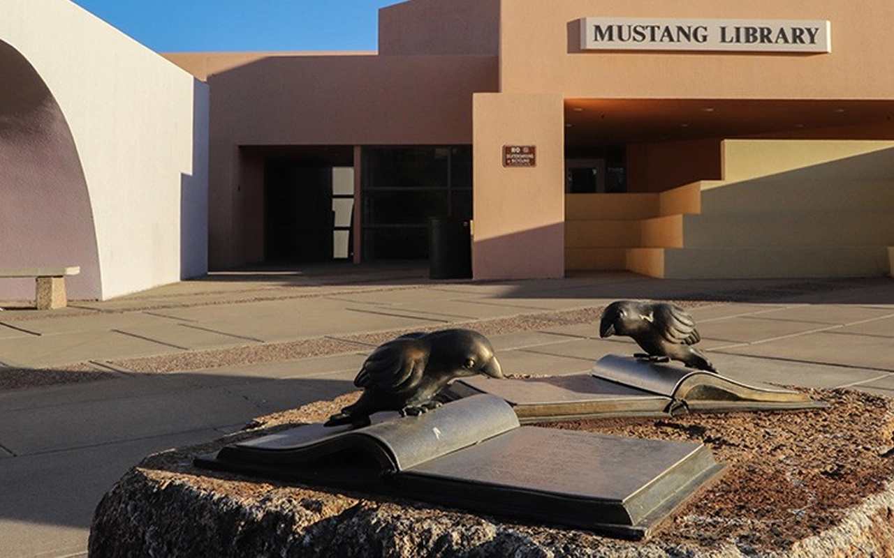 metal birds reading metal art book in front of library