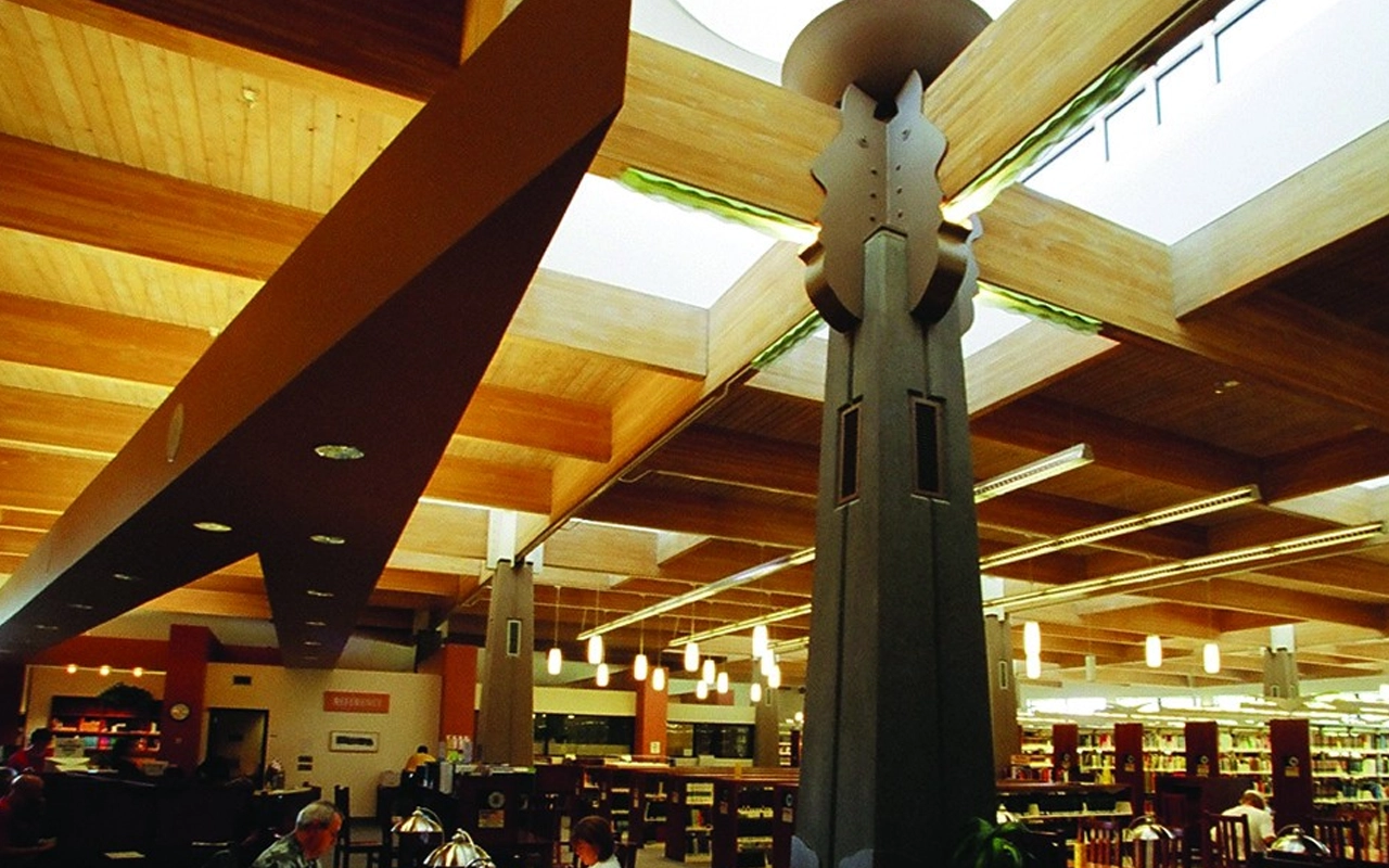 Modern library interior with wooden beams, skylights, and tall dark support columns.